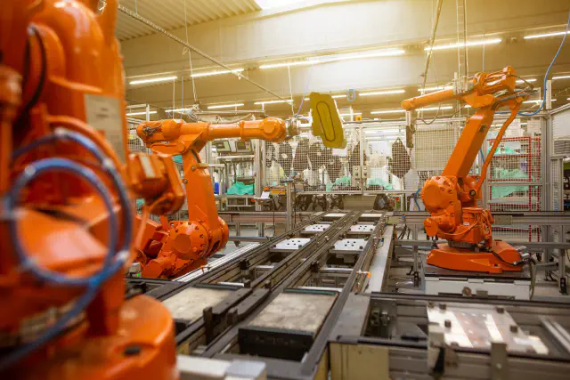 Large, heavy automated robots at a factory conveyor assembly line. The security of such operational technology is vital to ensure safety and business continuity.